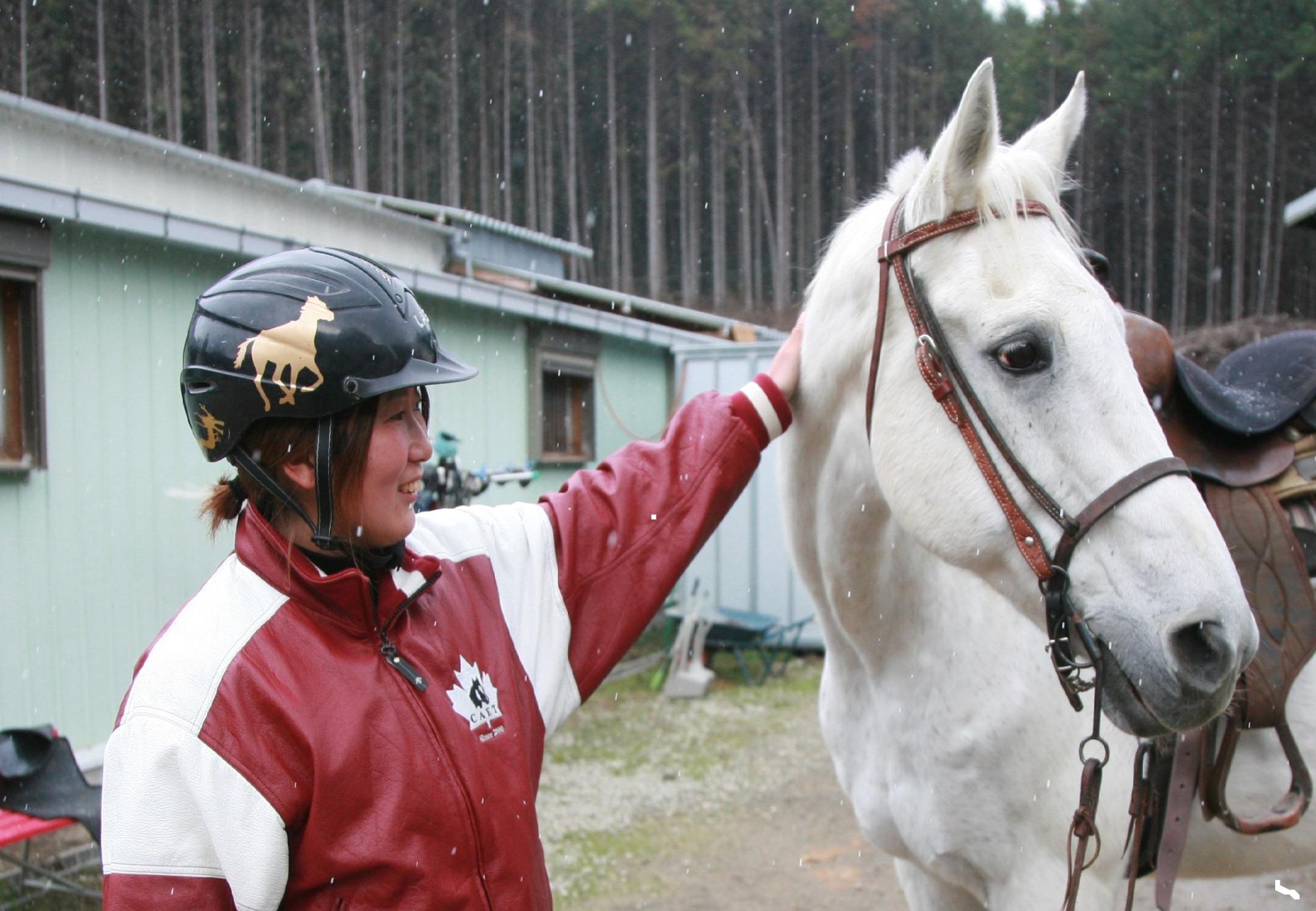 優しく微笑みながら白馬のタテガミを撫でている中山美香さんの写真