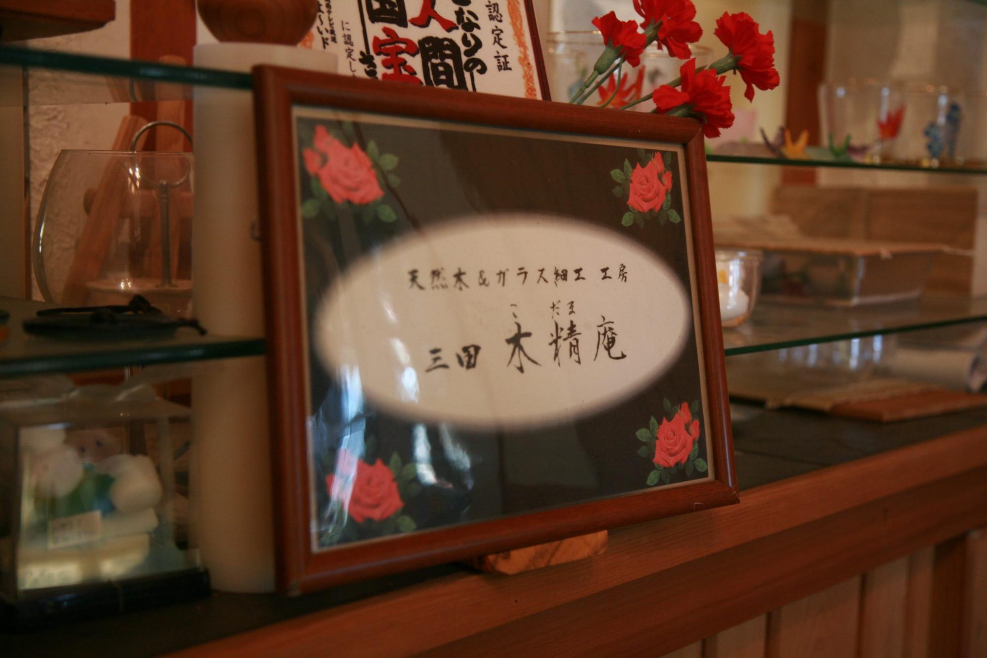 「天然木&ガラス細工 工房 三田木精庵(こだまあん)」と工房の名前が記載されたガラス製ネームプレートの写真