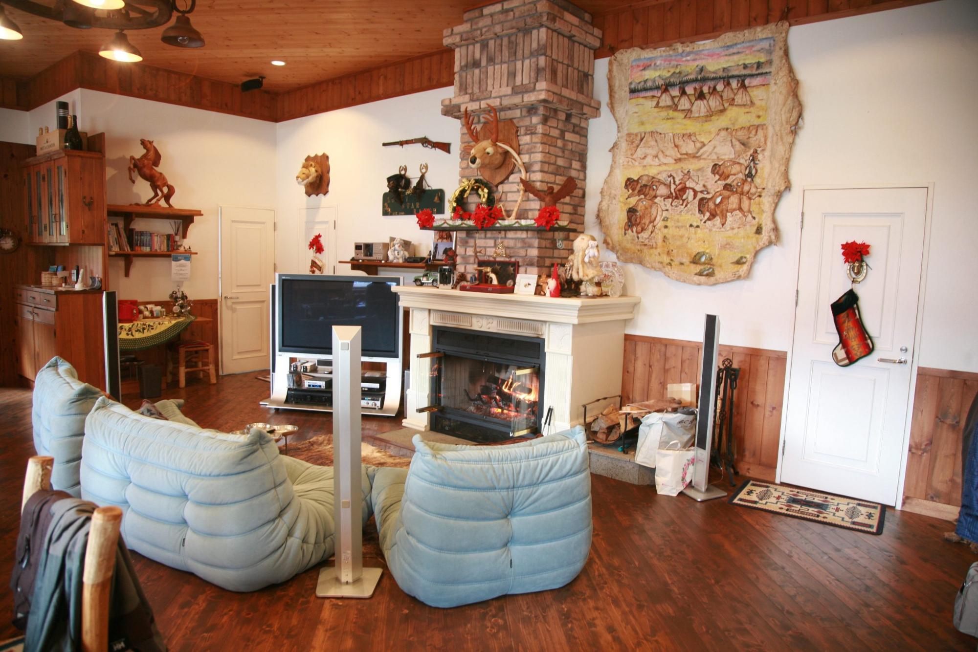 奥の壁面に暖炉、その右にテレビが設置され、その向かいに白い一人掛けのソファが3脚並んでいるカナディアンキャンプ乗馬クラブ神戸の休憩室の写真