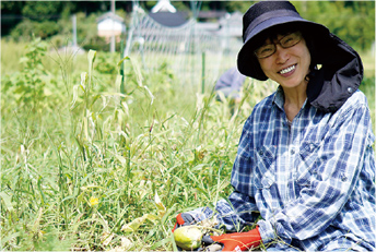 田畑を背景に、三田市で採れた収穫物を手にしてほほ笑む坂本 薫（さかもと かおる）さんの写真