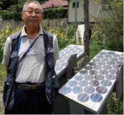 ミニ太陽光発電パネルの前に立つ佐藤 修一（さとう しゅういち）さんの写真