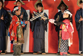 子供たちが着物を着て刀を打ち合わせている「お練り」の儀式の写真