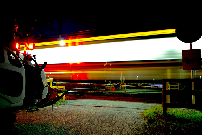 閃光を放って踏切の傍を走っていく夜の電車の写真
