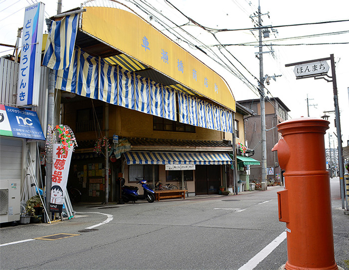 円筒型の赤いポストとその奥に見える古いお店の写真