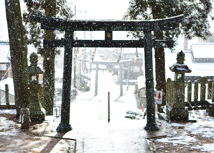 神社の鳥居の向こうに雪が降っている写真