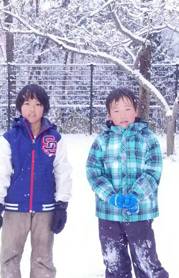 ブルゾンを着た女の子とチェックのシャツを着た男の子が雪降る中にいる写真