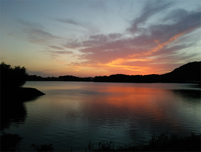 おだやかな湖面と、遠くで赤く色づく夕焼けの写真