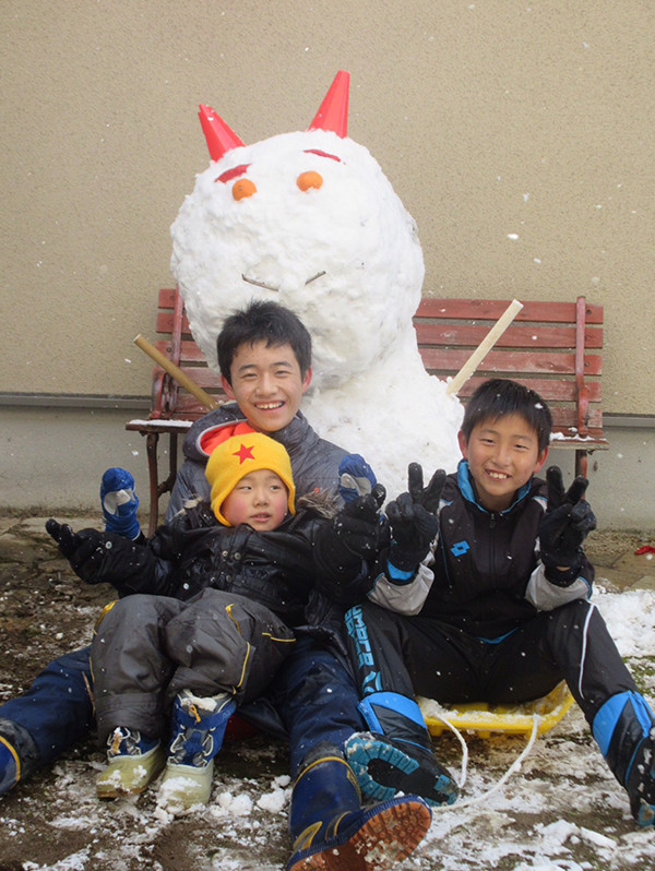 鬼をかたどった雪だるまとその前で微笑む3人の子どもたちの写真